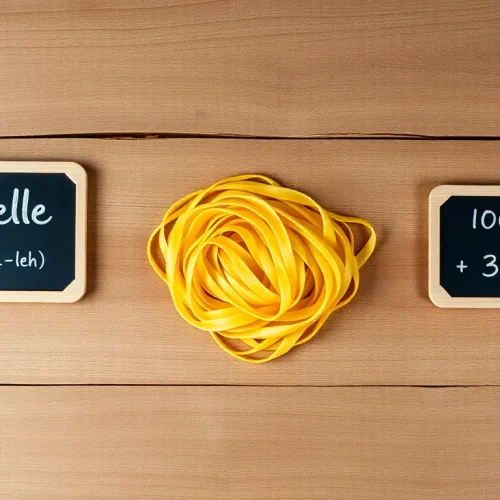 Włoski makaron tagliatelle, jego poprawna wymowa i informacja o kaloriach (kcal) zapisane na tabliczkach.